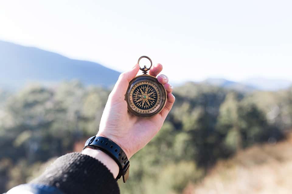 A person holding a vintage compass with a mountainous landscape in the background.